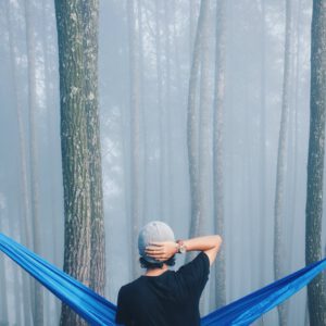 person sitting on blue hammock surrounded with tall trees