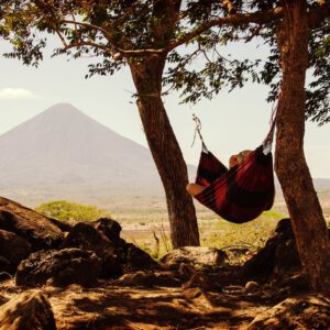 person lying on black and red hammock beside mountain under white cloudy sky during daytime